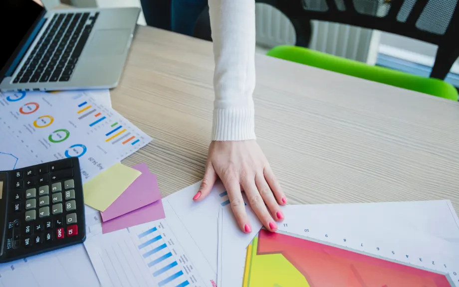 Persona analizando informes financieros y gráficos en un escritorio con calculadora y ordenador portátil