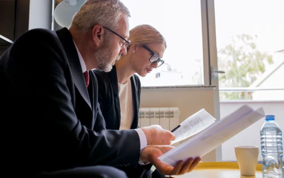 Dos profesionales con traje revisan documentos en una oficina