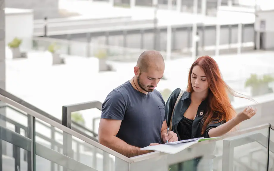 Dos jóvenes colaborando y tomando notas en un cuaderno en un espacio exterior